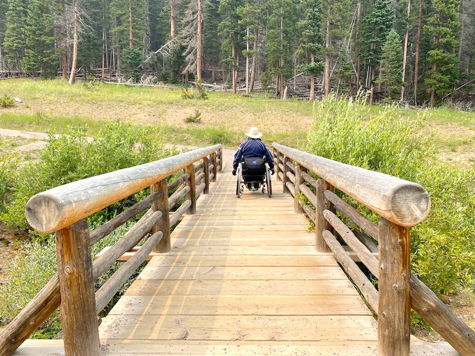 Person using a manual wheelchair crossing a wooden bridge